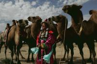 伝統的な民族衣装で身を包んだ女性がラクダのレースをみる。